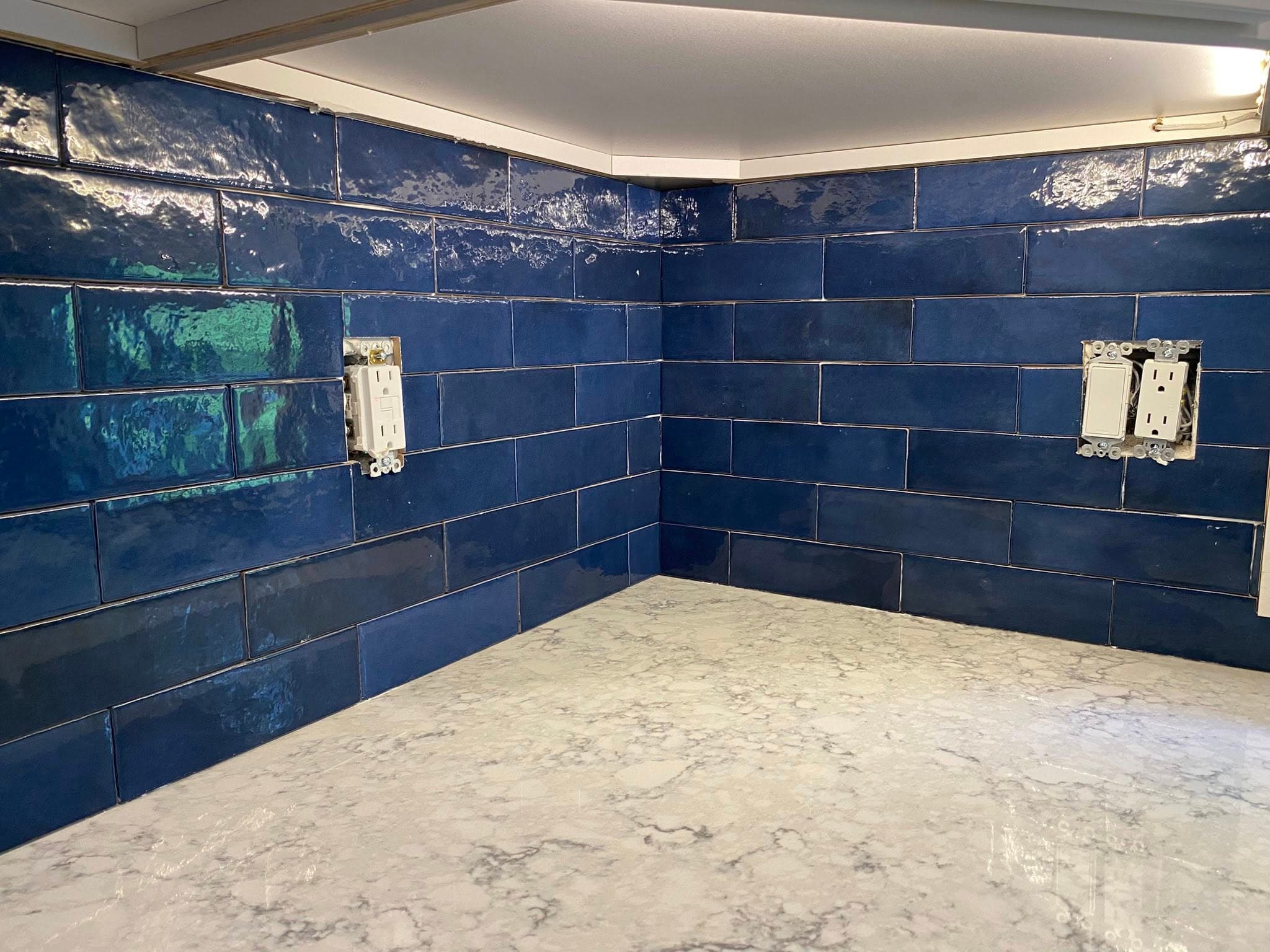 Glossy navy tile kitchen backsplash above a marbled quartz countertop