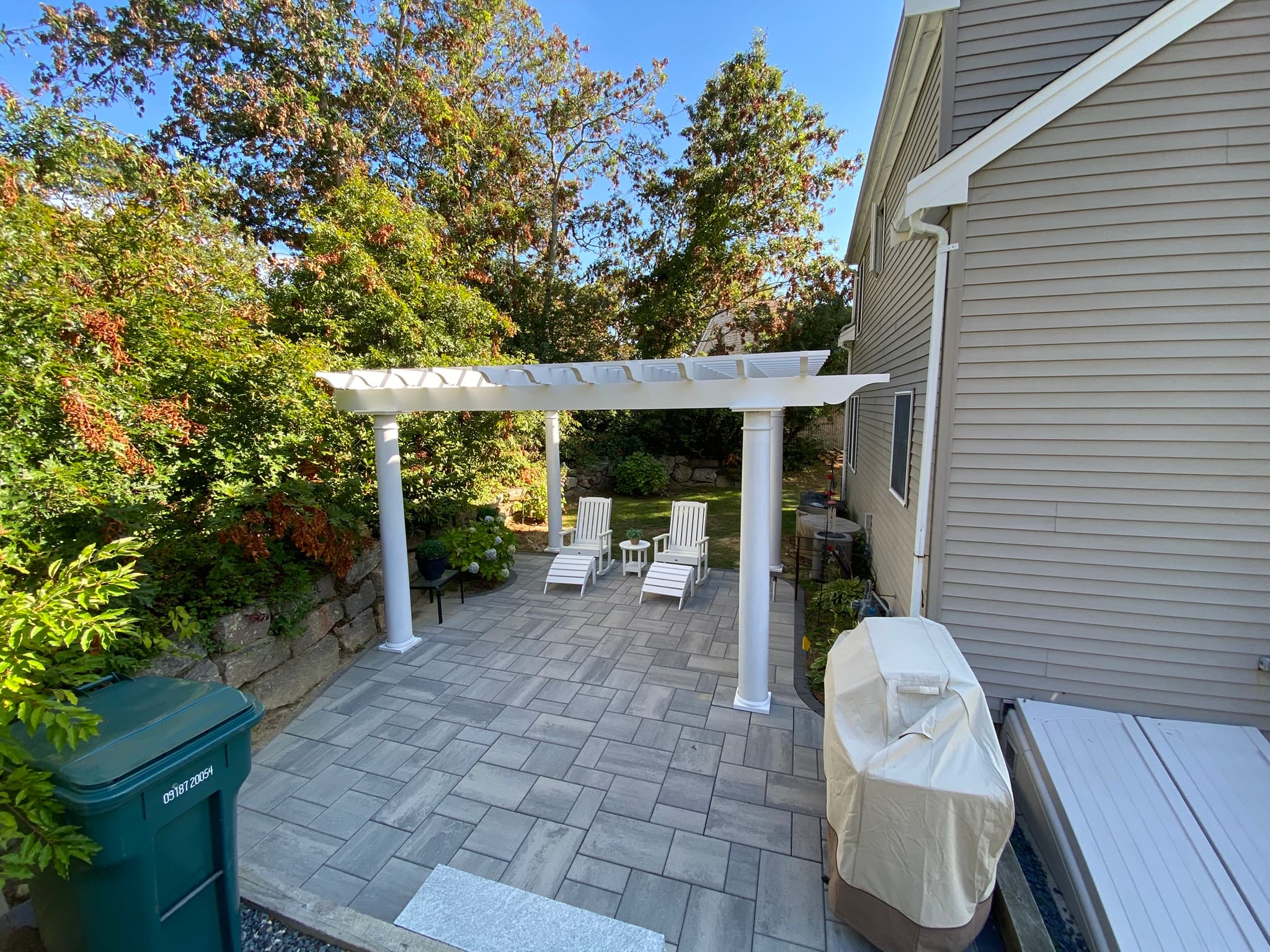 White pergola over paver patio with Adirondack chairs